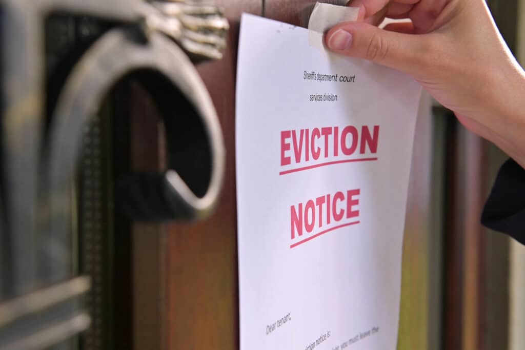 A landlord-tenant lawyer places an eviction notice on the wooden door, right next to the metal door knocker, as tensions from tenant disputes reach a boiling point.