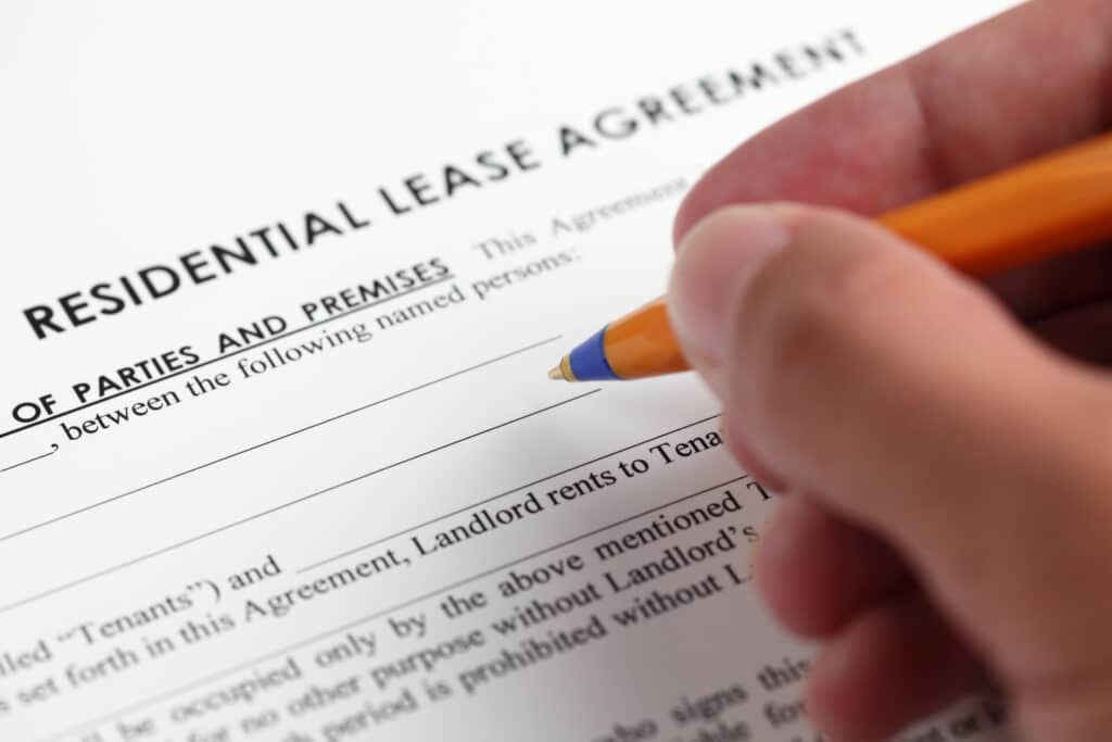 A hand holding a pen carefully fills in a residential lease agreement form, ensuring clarity for both tenants and landlords.