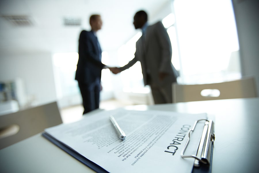 two business people shaking hands in the background with a contract on the table