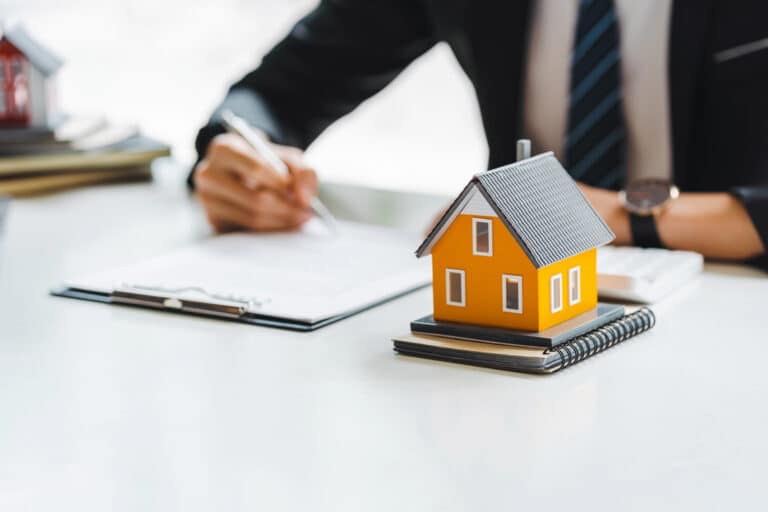A person in business attire signs documents at a desk with a model yellow house, highlighting how executors can avoid common mistakes during probate.